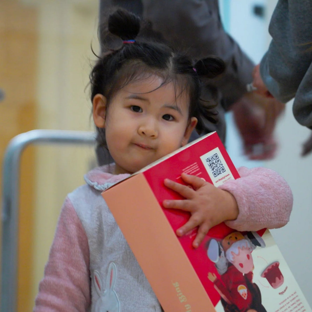 Young Asian American girl hugging a Jilly Bing 14-inch doll donation box at a community toy donation event.